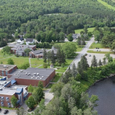 On some hills covered in trees next to a river, an overhead view of brick buildings.