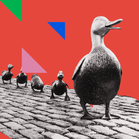 A statue of a mother goose with a trail of ducklings behind her. A triangular pattern in bright colors just left of the ducklings.
