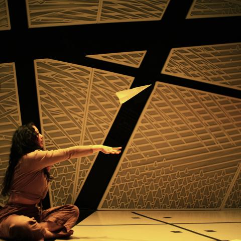In a room with padded walls, a woman throws a paper airplane.