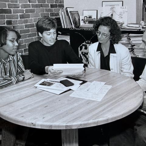 Four people sit around a round table. They look at papers together.