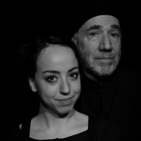 In black and white: a young white woman poses with an older white man in a beanie that fades into the black background.