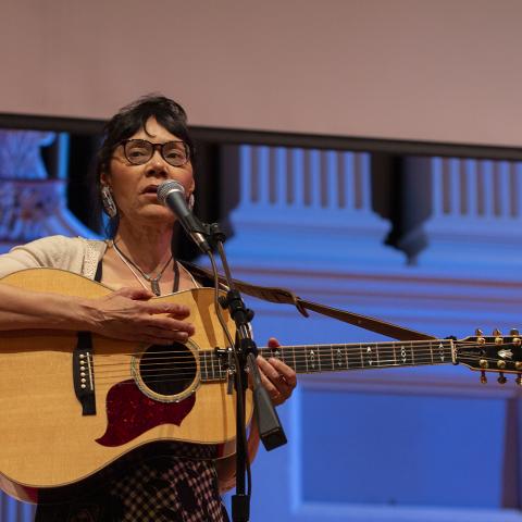 A woman playing a guitar singing into a microphone
