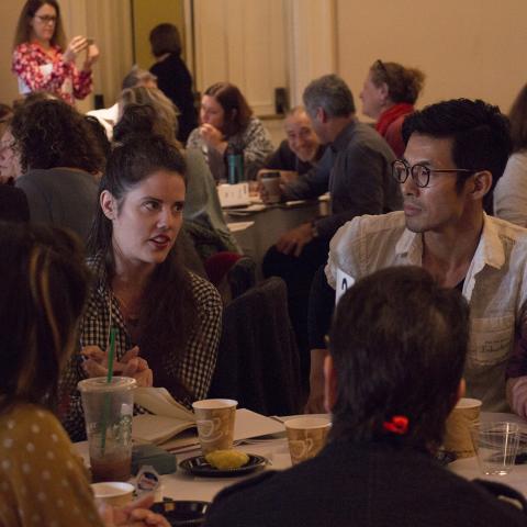 A group of young artists sit around a table having a discussion.