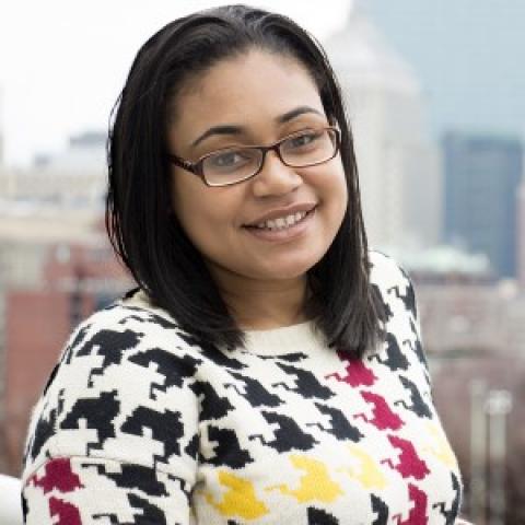 Azia smiles in front of the Boston skyline in sweater with a large herringbone print.