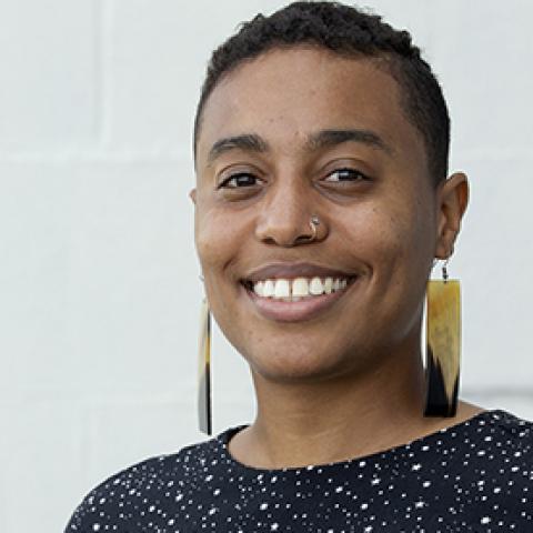 A smiling person with short hair and chunky earrings