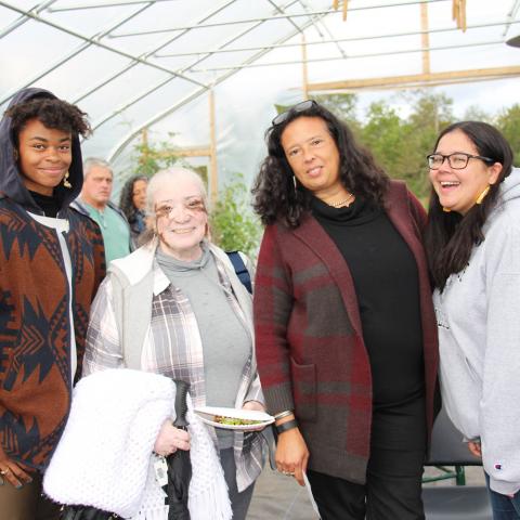 Artist Nia Holly (Nipmuc), Gail Rokotuibau (Narragansett/Pequot), Dawn Spears (Narragansett/Choctaw), and Samantha Fry (Narragansett) stand together and smile facing the camera inside a high tunnel at the Markets & Marketing workshop