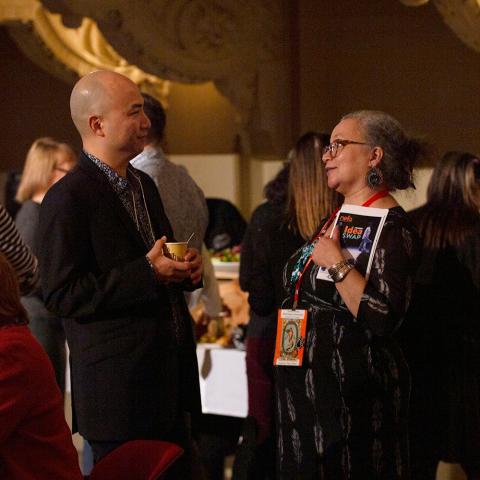 An Asian man and woman of color chat while holding the Idea Swap brochure.