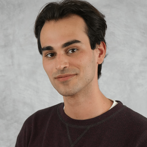 Joaquin poses in front of a gray backdrop. He has short brown hair and wears a maroon sweater.