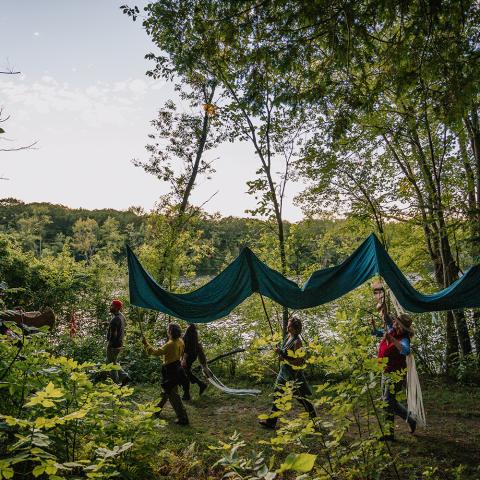 On a trail in daylight, a group of people parade a curtain of fabric.