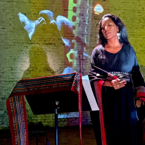 A woman, in a wrap dress, reads from a music stand that has a similar fabric as her dress across it.