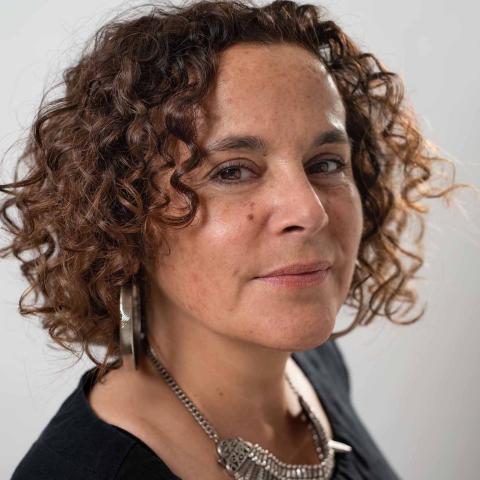 A woman with brown curly hair wearing a black top, large silver earrings and an intricate silver necklace