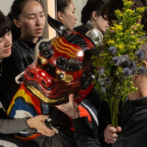 Folks, in black clothes, hold an east Asian dragon mask and leaves.