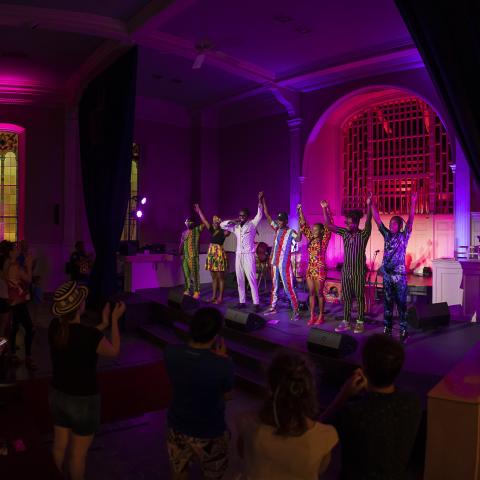 Panomrama of an audience and a band taking a bow on a stage.