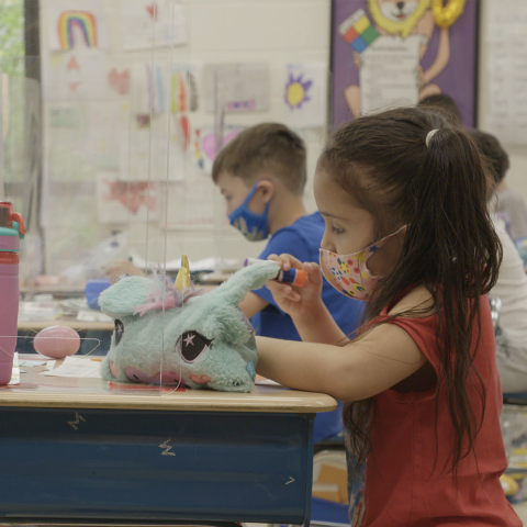 Young students wear N95 masks and sit at their desks.