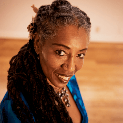 African woman with locked hair wearing a blue dress and black pearl necklace.