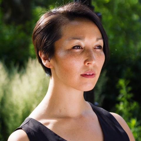 Outside, Michele has short hair and wears a black dress with a deep v-neck.