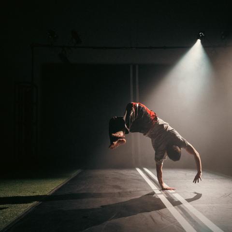 In a spotlight and on a road that appears to continue up the wall, a dancer does a flip.