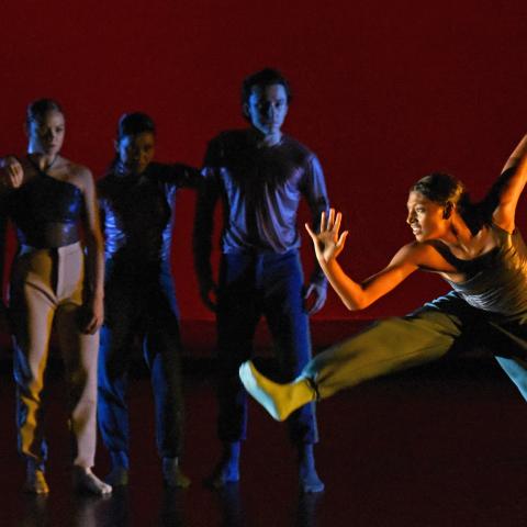 In a spotlight, a dancer leaps while four more dancers look in.