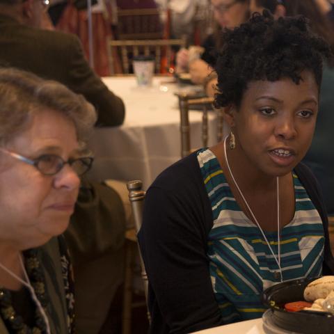 Two women, sitting at a banquet table, look to a person off camera.