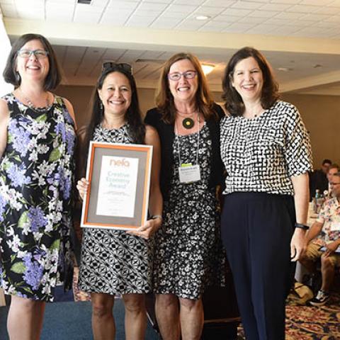 4 people stand shoulder to shoulder; one holds framed award that reads NEFA's Creative Economy Award