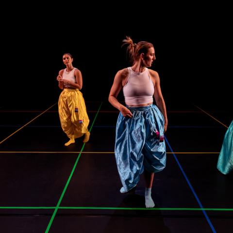 Four dancers, in monochrome, but each different, parachute pants, perform in a black box with the same colors as intersecting lines on the ground.
