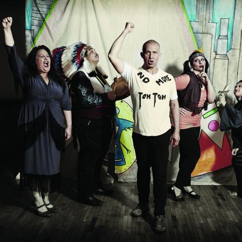 Five people stand in costumes in front of a hand drawn backdrop.