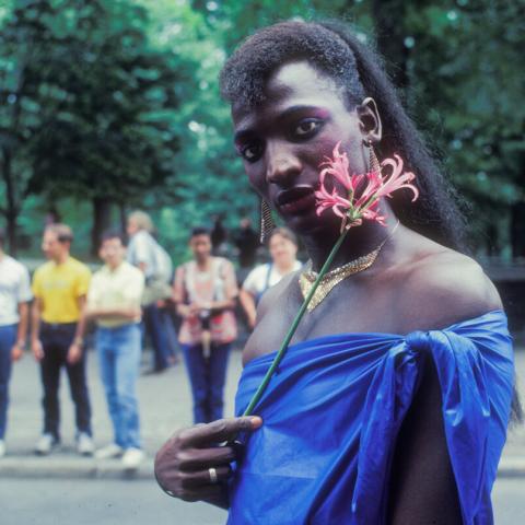 In a park, a Queer Black person holds a flower next to her face.