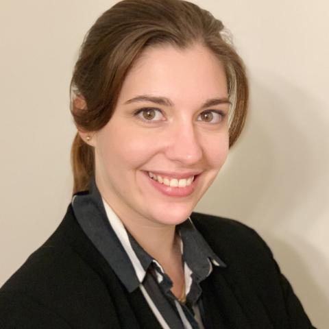 a woman with long hair pulled back wearing a black and white striped shirt and black blazer against a beige background