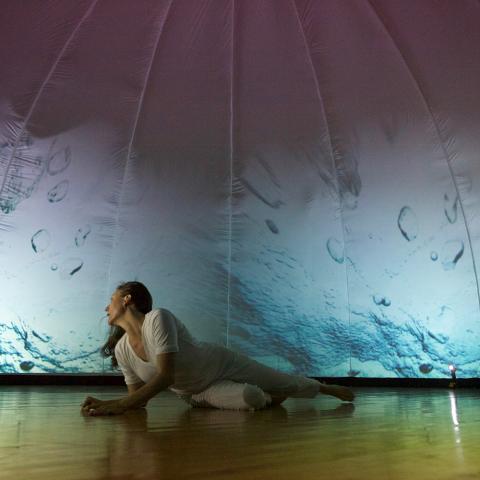 A woman lays on the ground, in front of a projection of water.