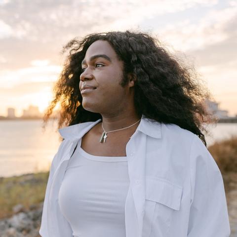 By a pond at sunset, Nia, a Black woman with long curly hair, looks off into the distance.