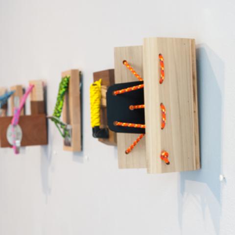 Wall mounted sculptures with yarn and string tethered to wood blocks.
