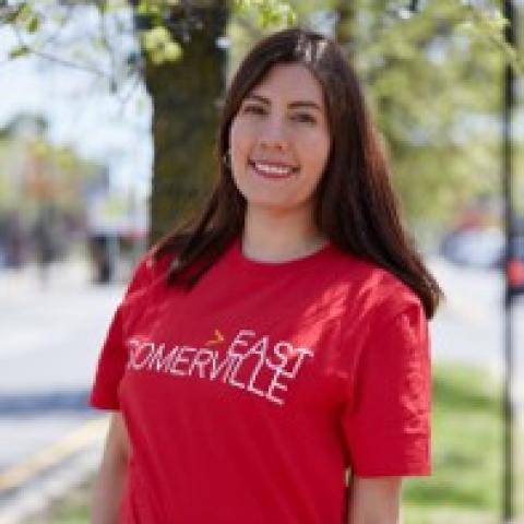 Paula has long brown hair. She has light skin and wears a red t shirt.