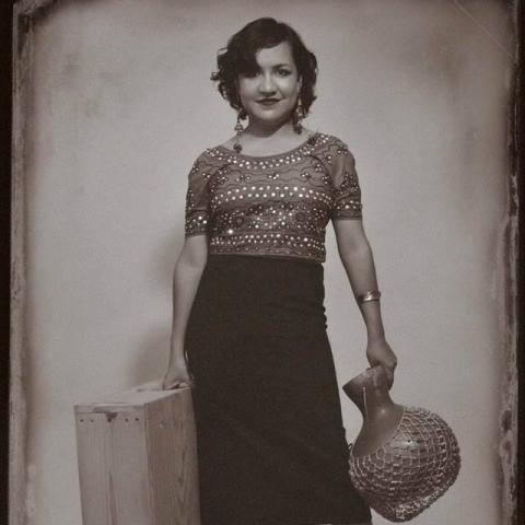 A woman poses with a vase and a suitcase.