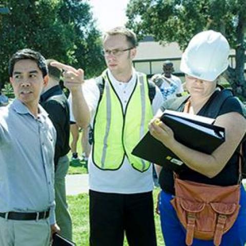 Four people are in a park. Two point off camera. One wears a hard hat.