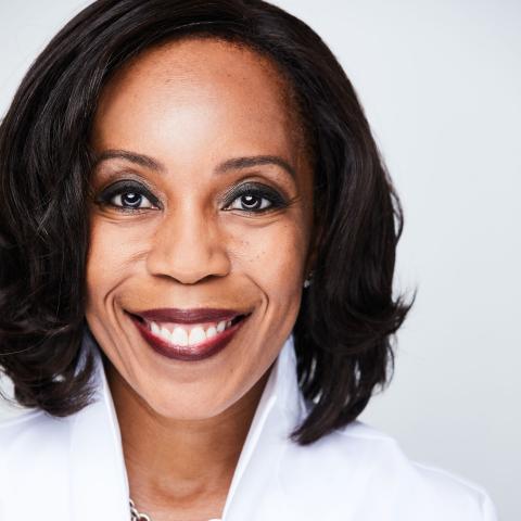 Renae is a Black woman with shoulder length brown hair. They wear a white blouse and smile brightly.