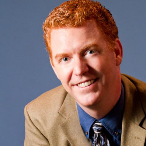 Charles leans forward in front of a blue-gray background