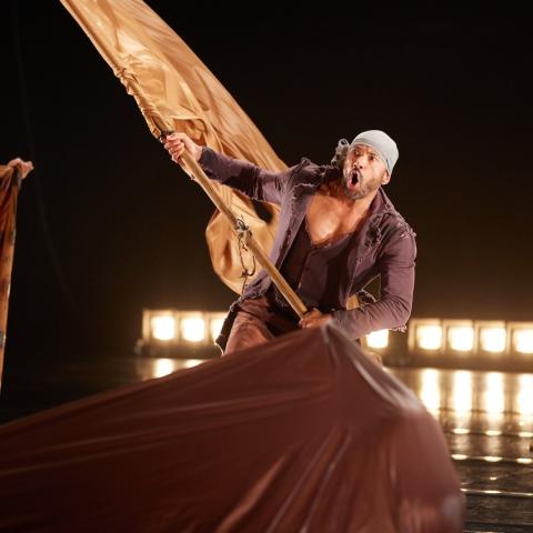 A man of color, in purple and a gray headwrap, waves a tan flag.