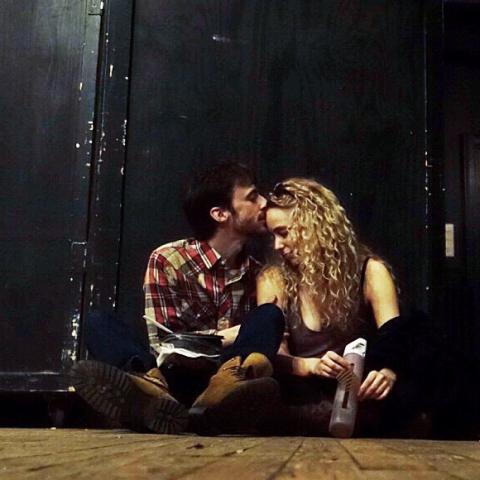Two folks sit on the floor and caress between two speakers.