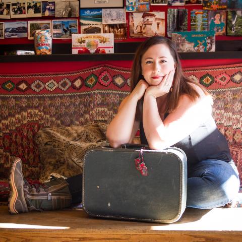 Sarah sits on the ground, leaning over a suitcase.