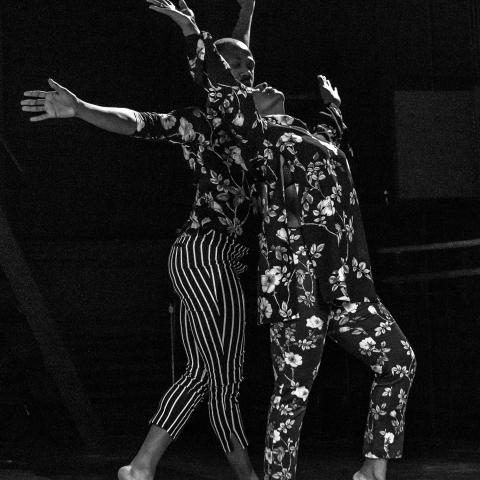 In black and white, two Black dancers perform in floral costumes.