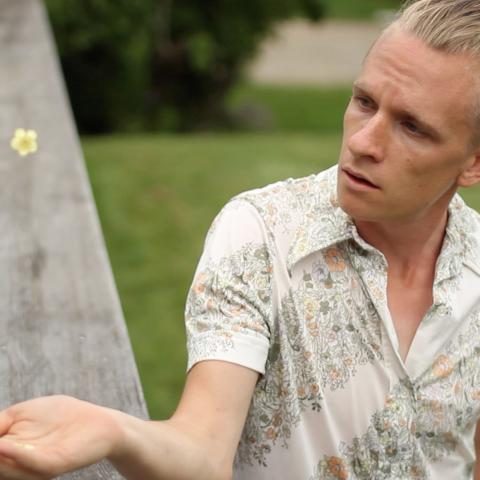 Scott holds his hand out to catch a flower. He has a blond bun.