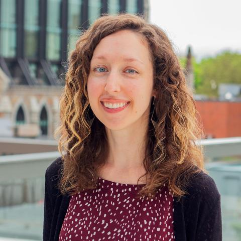 Sharon is a white lady with shoulder length brown hair with highlights. She's outside and she smiles in a maroon blouse with white polka dots.