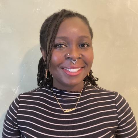 Sharon is a Black woman and she has shoulder length braids. She smiles and wears black and white stripes under a gold necklace.