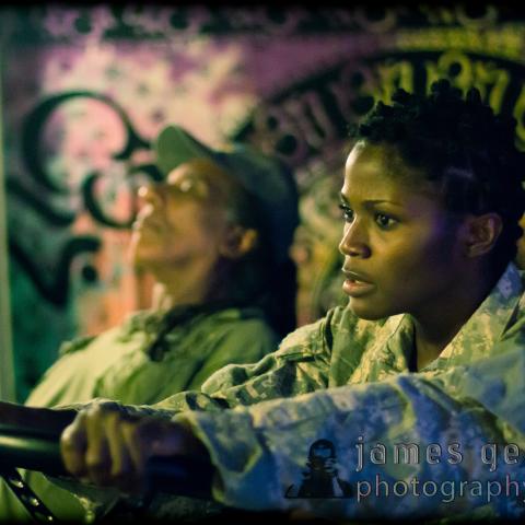 A female soldier drives while a male soldier rests in the passenger seat.