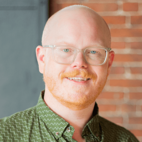 Steven is a bald white man. He has a ginger beard and wears a complimentary green button down.