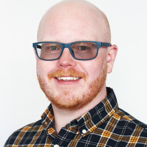 A white man, in glasses, has a short red beard and wears flannel.