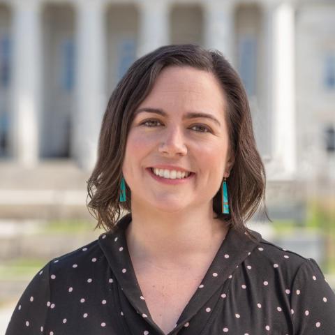 a white woman with brown shoulder length hair wearing long green earrings and a polka dot shirt.