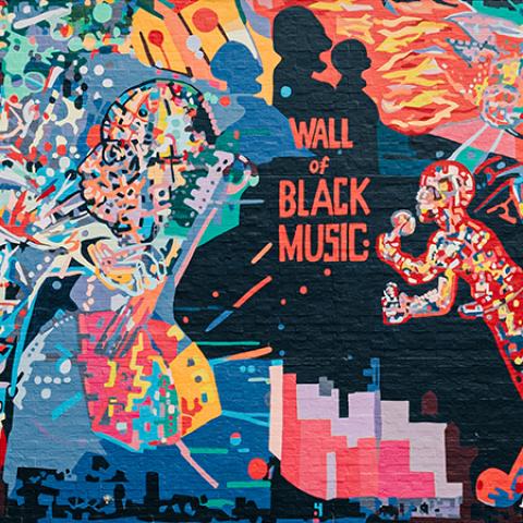 On the side of a building, a mural with folks in nonhuman hues playing brass instruments. "Wall of Black Music."