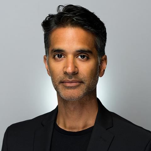 Vijay is a brown man. He is in studio lighting, a white space, and wears all black.