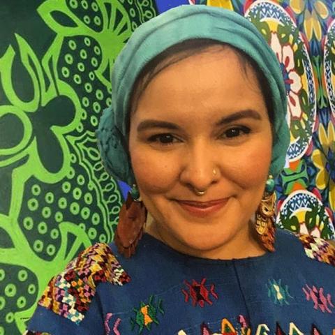 Betsy wears a headwrap. She has light skin and wears a floral print.